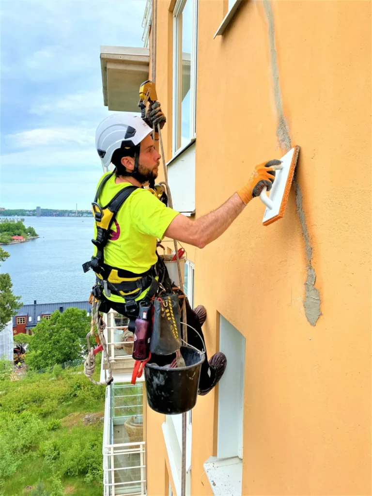 En person utför fasadrenovering via rope access.