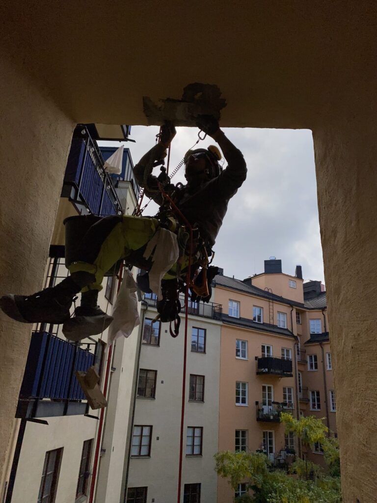 En person hängder i rep och utför fasadputs via reparbete.