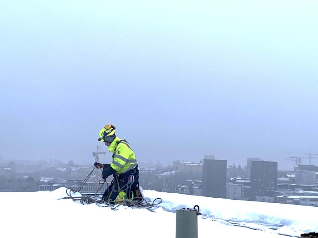 En man utför konsultation av personsäkerhet under vintern på ett tak. 